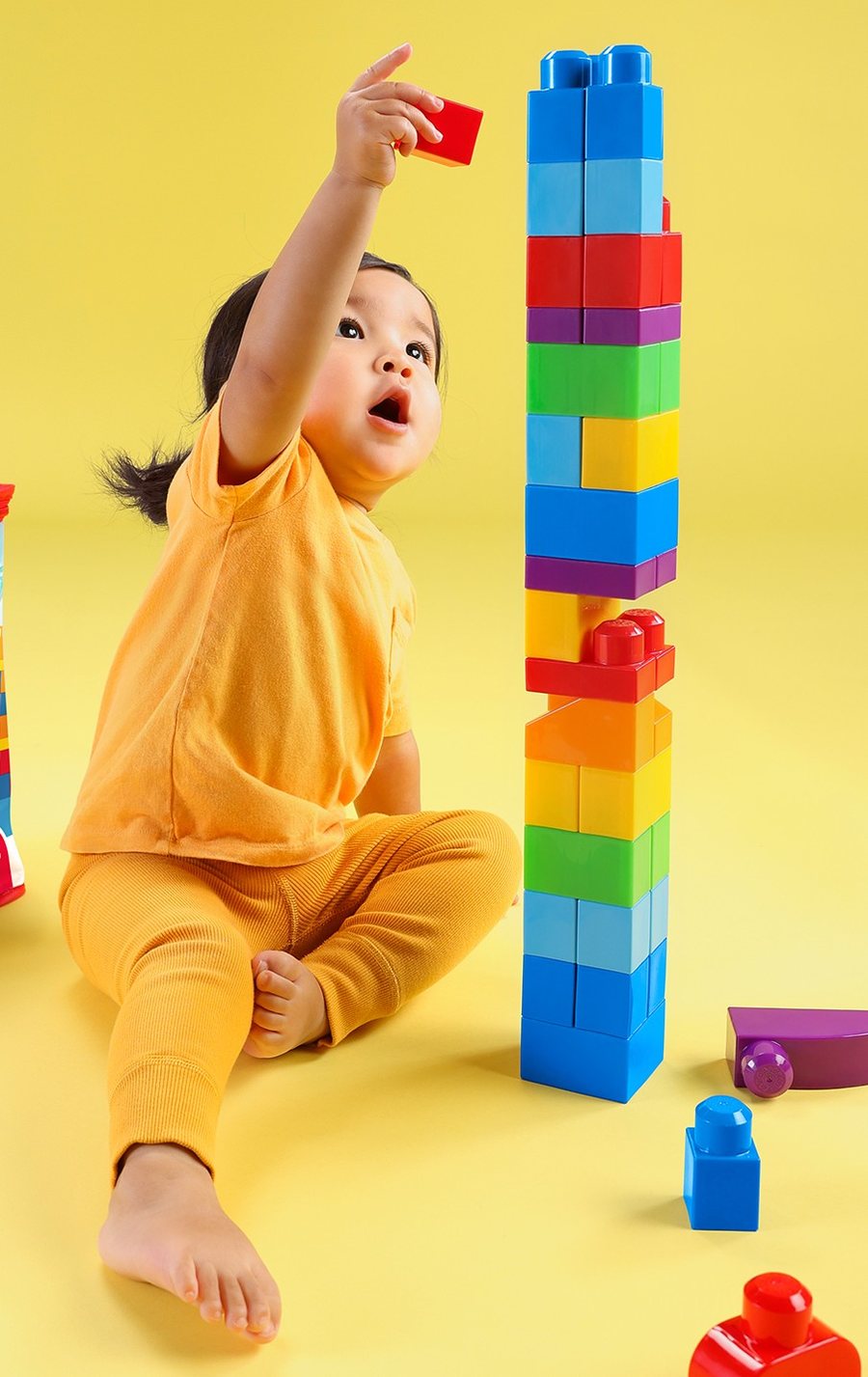 Toddler stacking a tall tower of colourful MEGA BLOKS blocks
